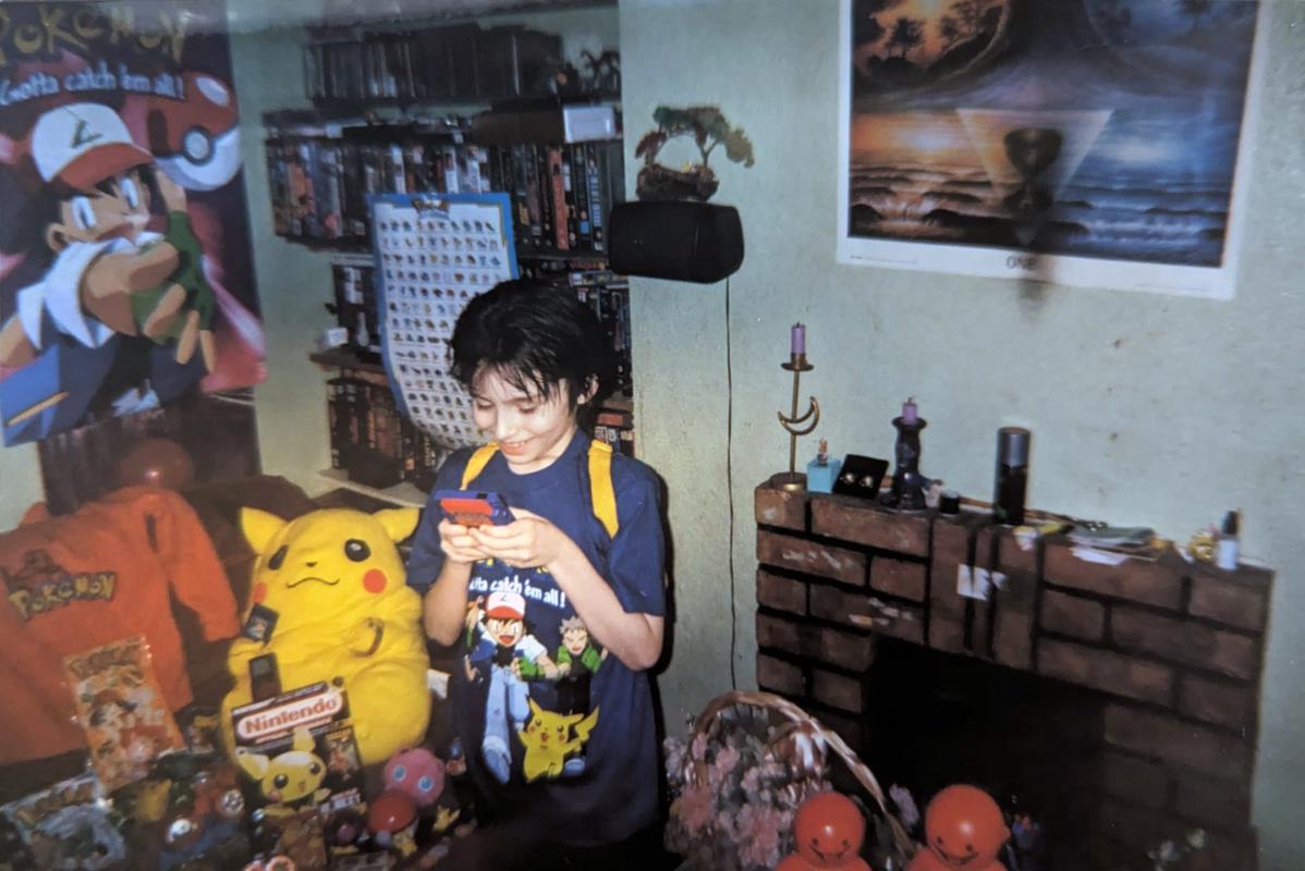 A photograph of Dazz playing Pokémon Red on his Game Boy Color, surrounded by lots of classic Pokémon toys and merchandise