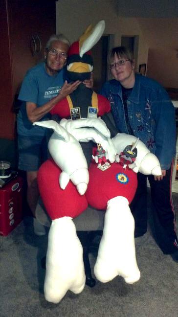 A photograph of Jay’s mother and grandmother, along with a giant Bisharp plush, with smaller plush toys and Pokémon trading cards