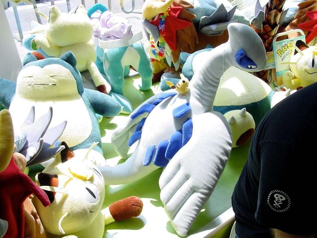 A photograph taken inside the store, showing the window display from behind. Here, we can see even more plush toys, such as Meowth, and a Pikachu on top of Lugia’s back