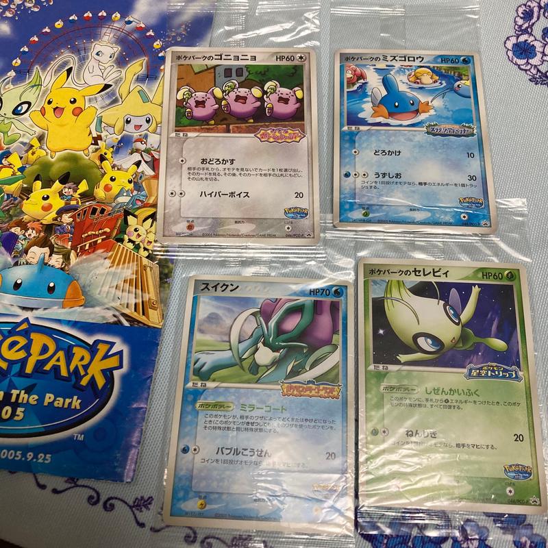 Shiori's Pokémon the Park promo cards, featuring Whismur, Mudkip, Suicune, and Celebi. Next to it, is a pamphlet from the park